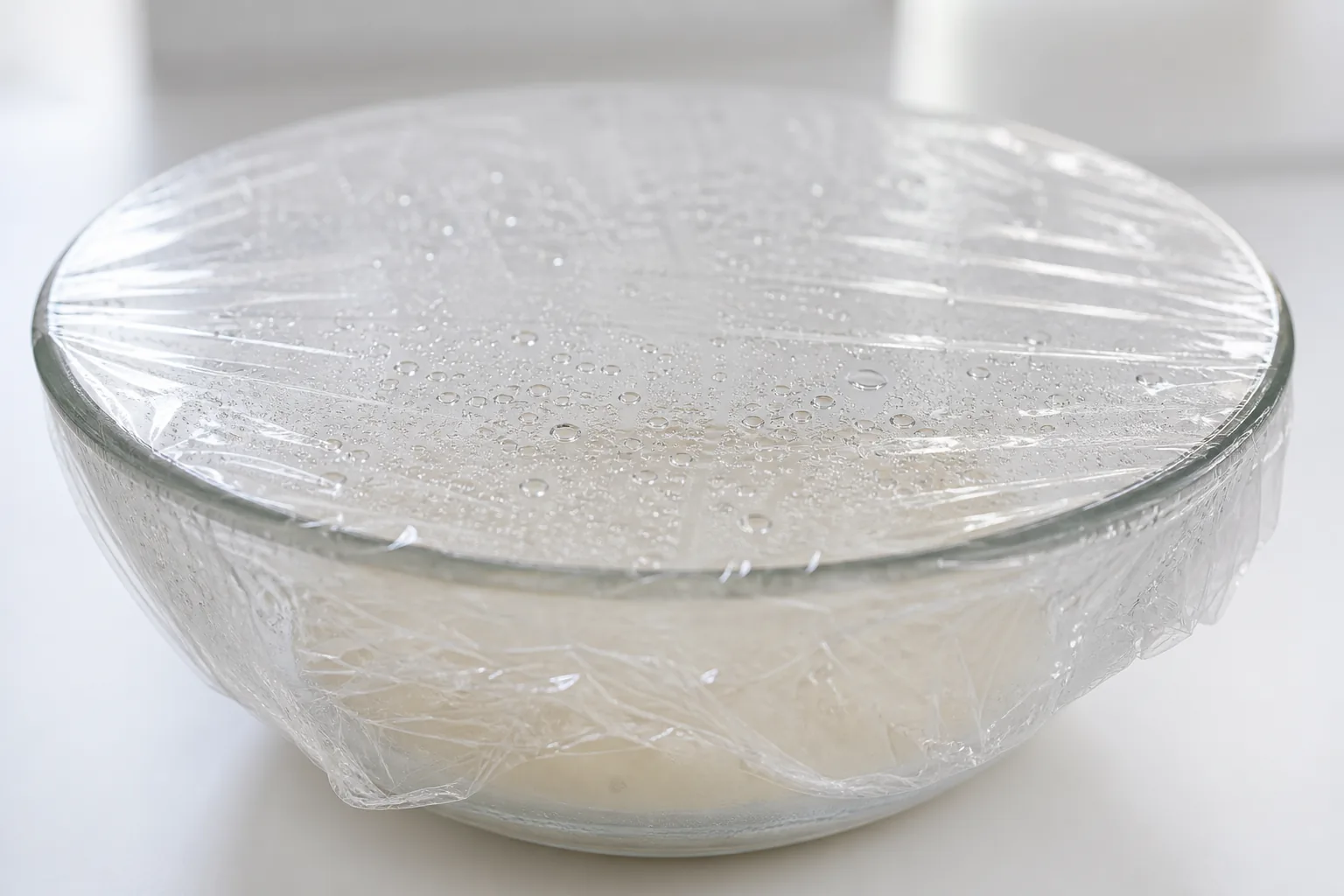 Clear plastic food wrap stretched over a glass bowl specimen in a food-contact materials laboratory.